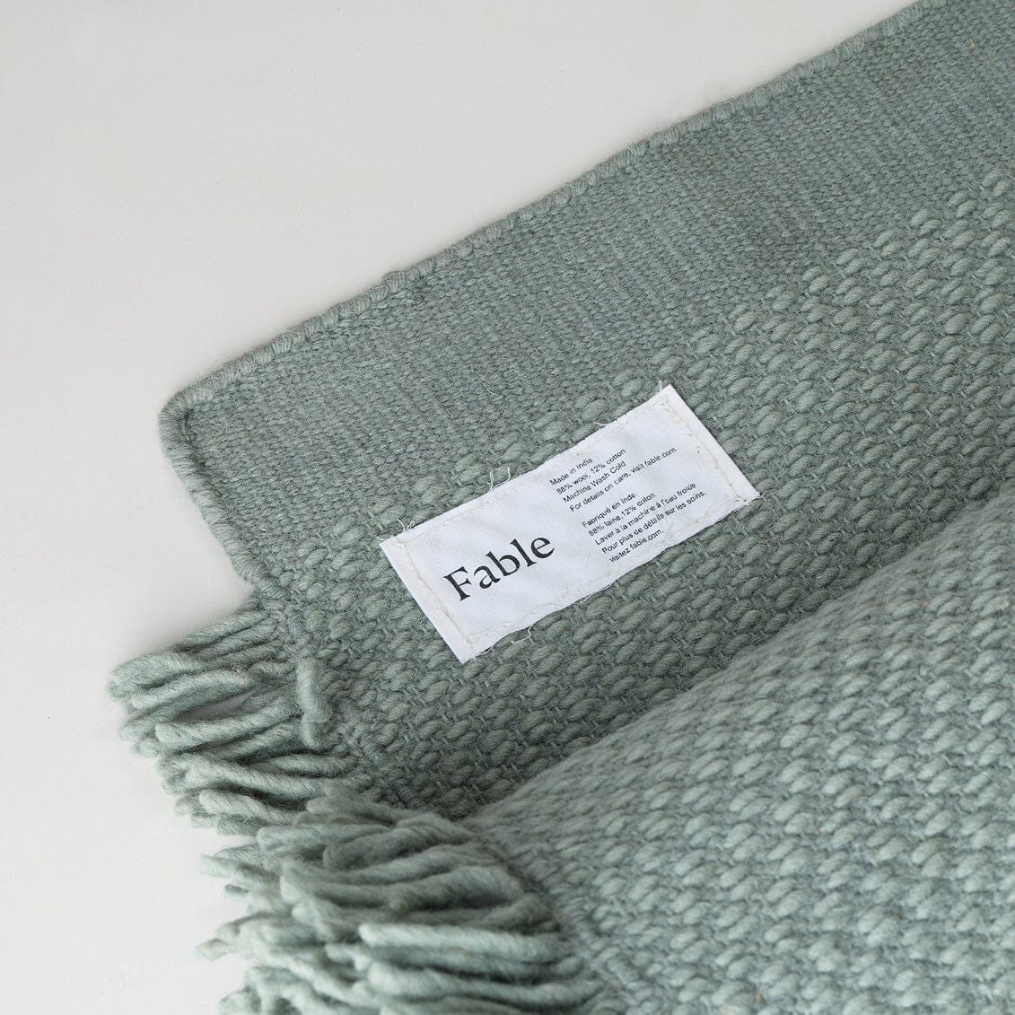 Green woven blanket with a 'Fable' label on a white background #sagegreen