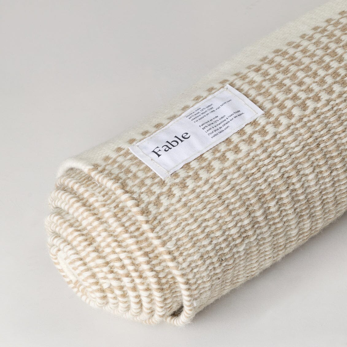 Rolled-up beige blanket with a label on a light gray background #coastalcream