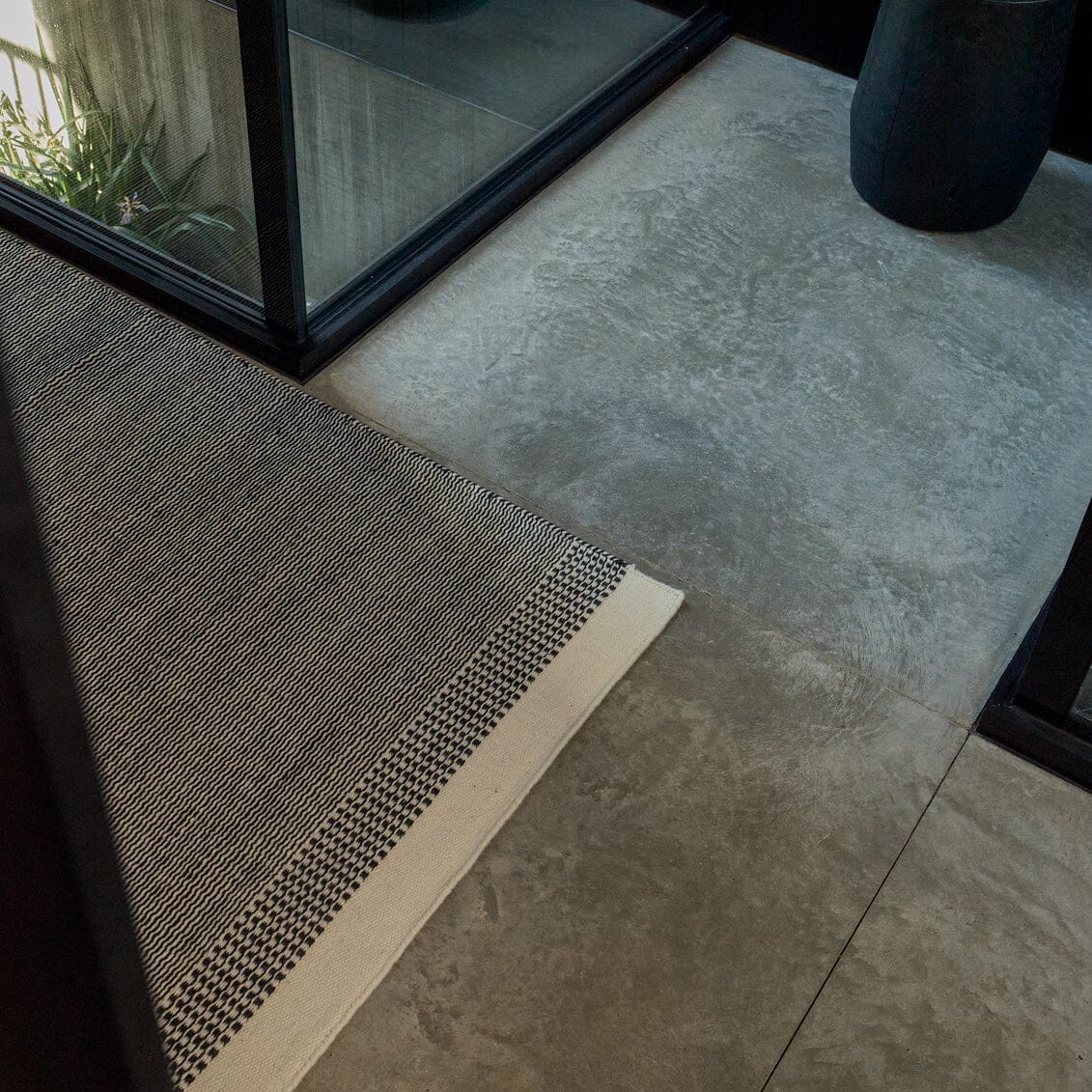 Textured doormat on a tiled floor with a mirror reflecting indoor plants. #ashblack