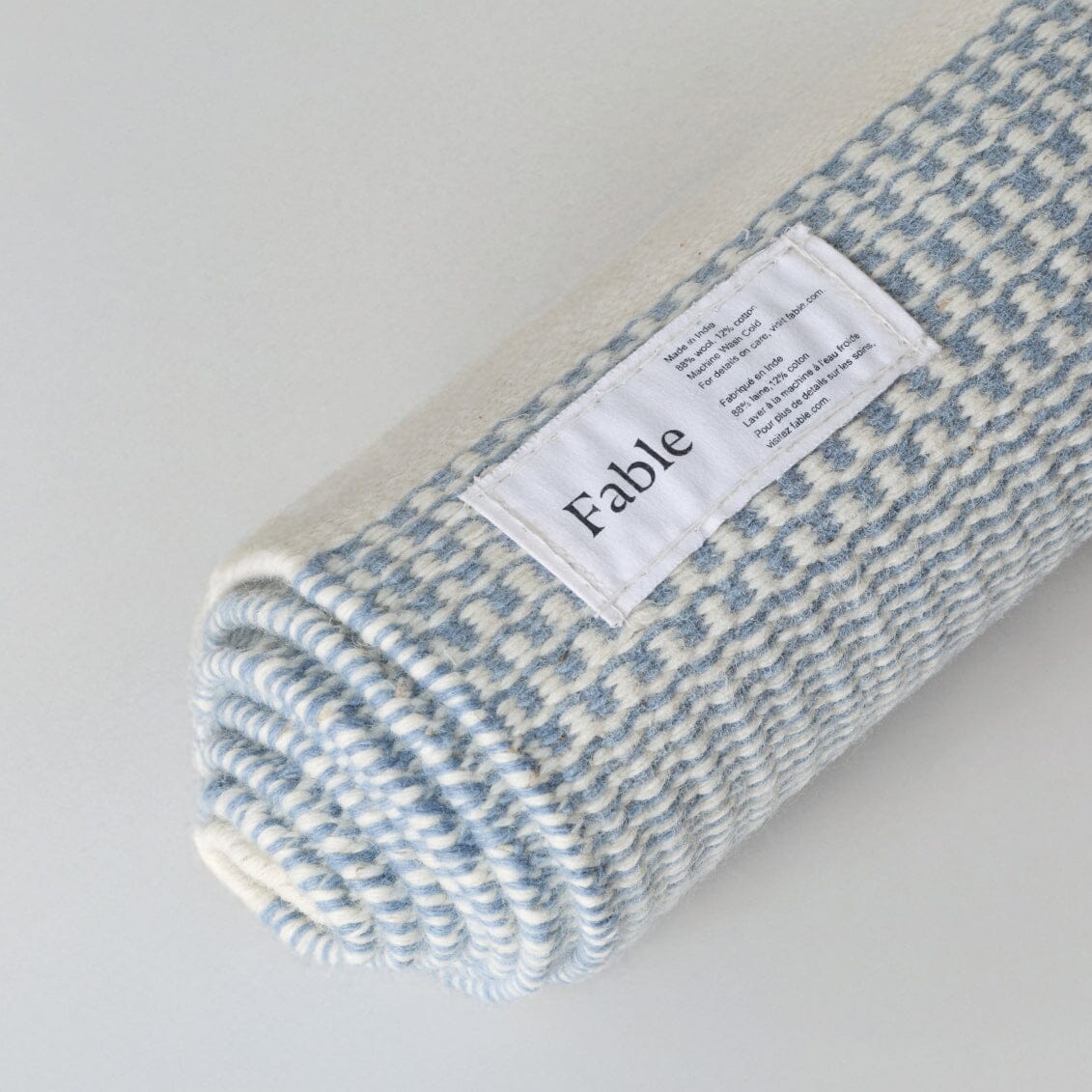 Folded blue and white checkered blanket with a label on a light gray background #duskblue
