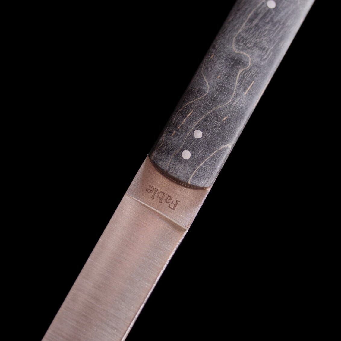 Close-up of a knife blade with a branded handle on a black background